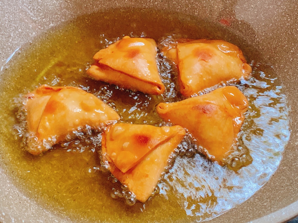5 homemade Samosas are being fried in a Wok